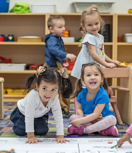 Collaborative Art — Pre-K Childcare Program in Skyway Pre-K children drawing together on large floor paper in a bright classroom with open shelves — Pre-K Childcare Program in Skyway.